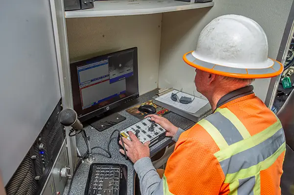 Man wearing hard had and reflective gear uses joysticks while looking at a screen