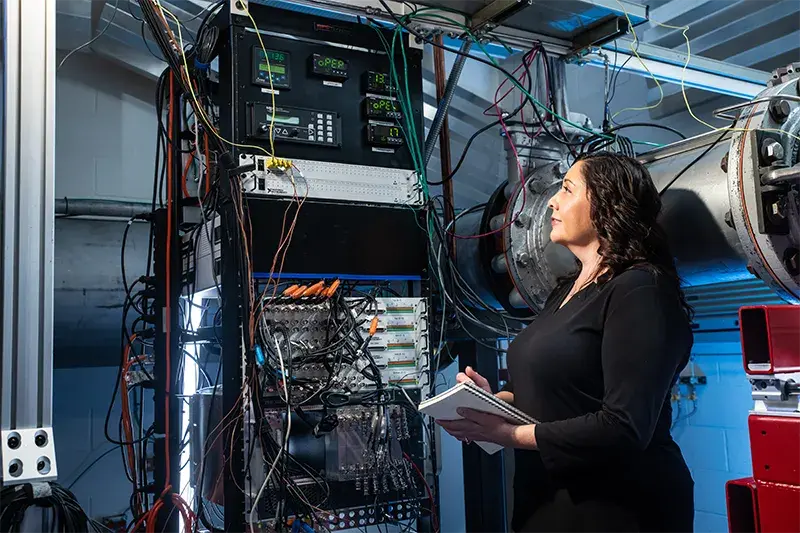 Woman writes on tablet as she inspects the results showing on a large machine with different colored wires connected to it