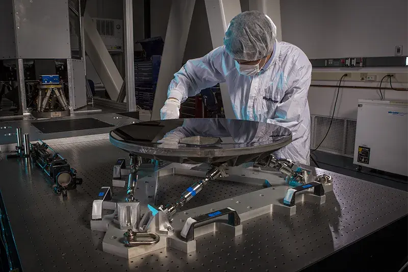 Man in dust protection gear works on an apparatus with metal bars holding up a reflective disk