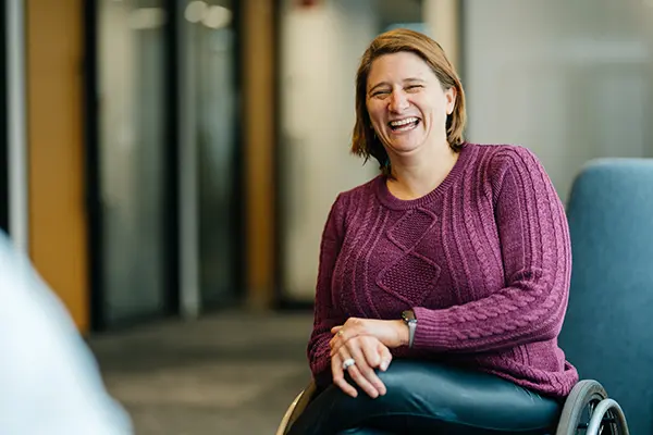 woman wearing sweater and short bobbed hair in wheelchair in open lounge area laughing