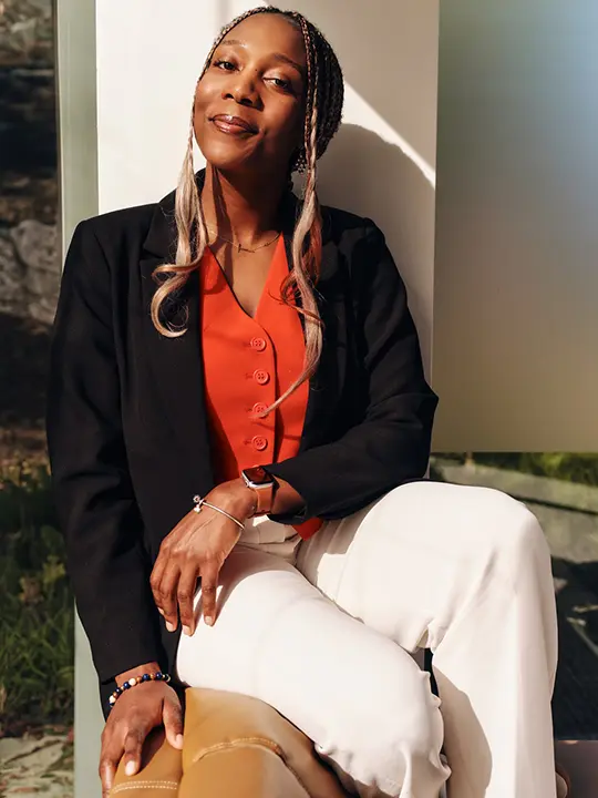african american woman in professional attire and long twisty braids sits in top back of a sofa smiling in the sun
