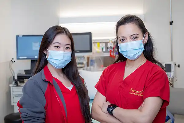 women in red scrubs and surgical masks in nurse's staions standing in front of files and computers
